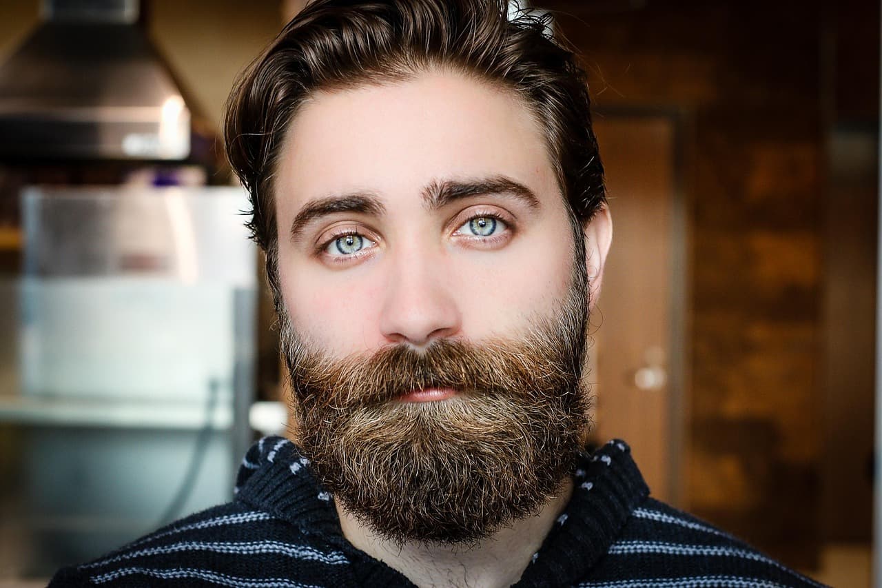 A man with a full, neatly shaped beard and swept-back hair